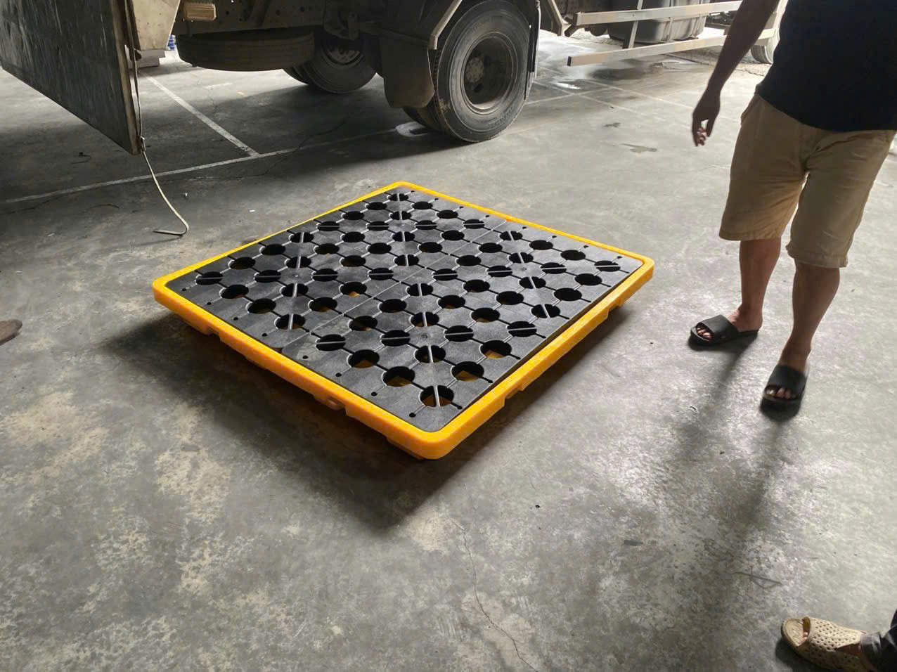Pallet nhựa màu vàng đen đặt trên nền kho, dùng để kê hàng hóa trong vận chuyển và lưu trữ
