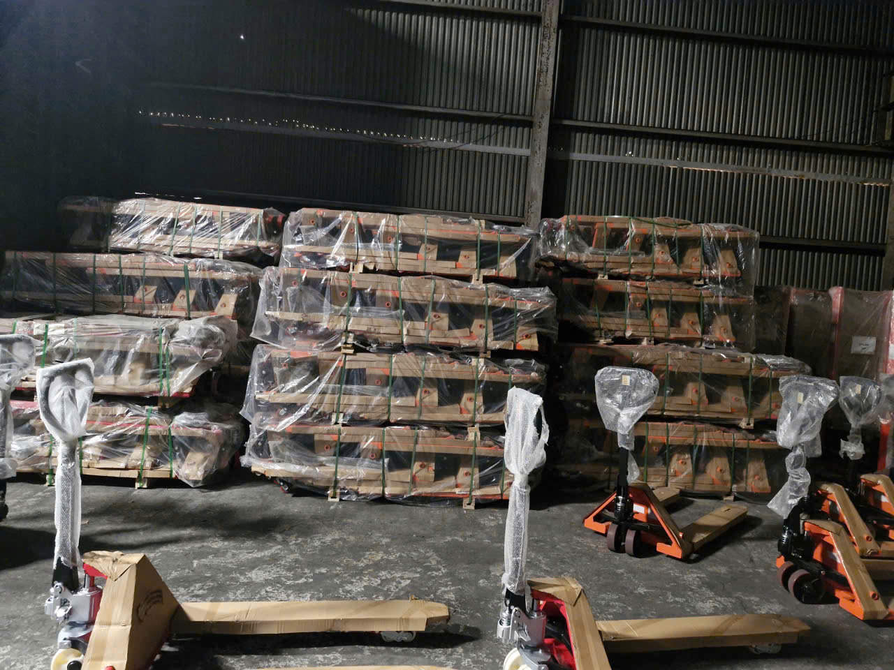 Xe nâng tay và pallet hàng được bọc nilon xếp chồng trong kho chứa hàng
