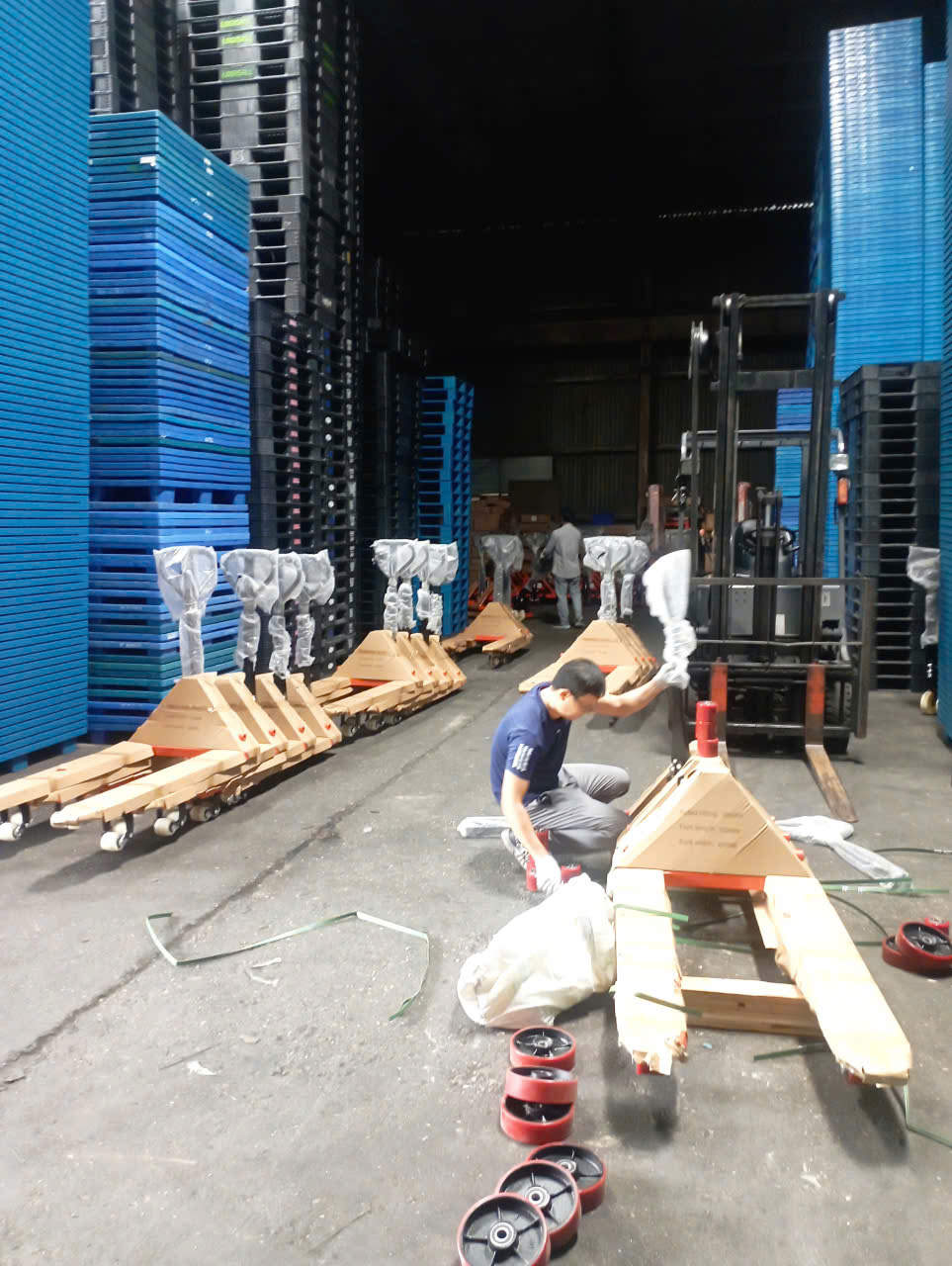 Nhân viên lắp ráp xe nâng tay thủy lực trong kho chứa nhiều pallet nhựa xanh