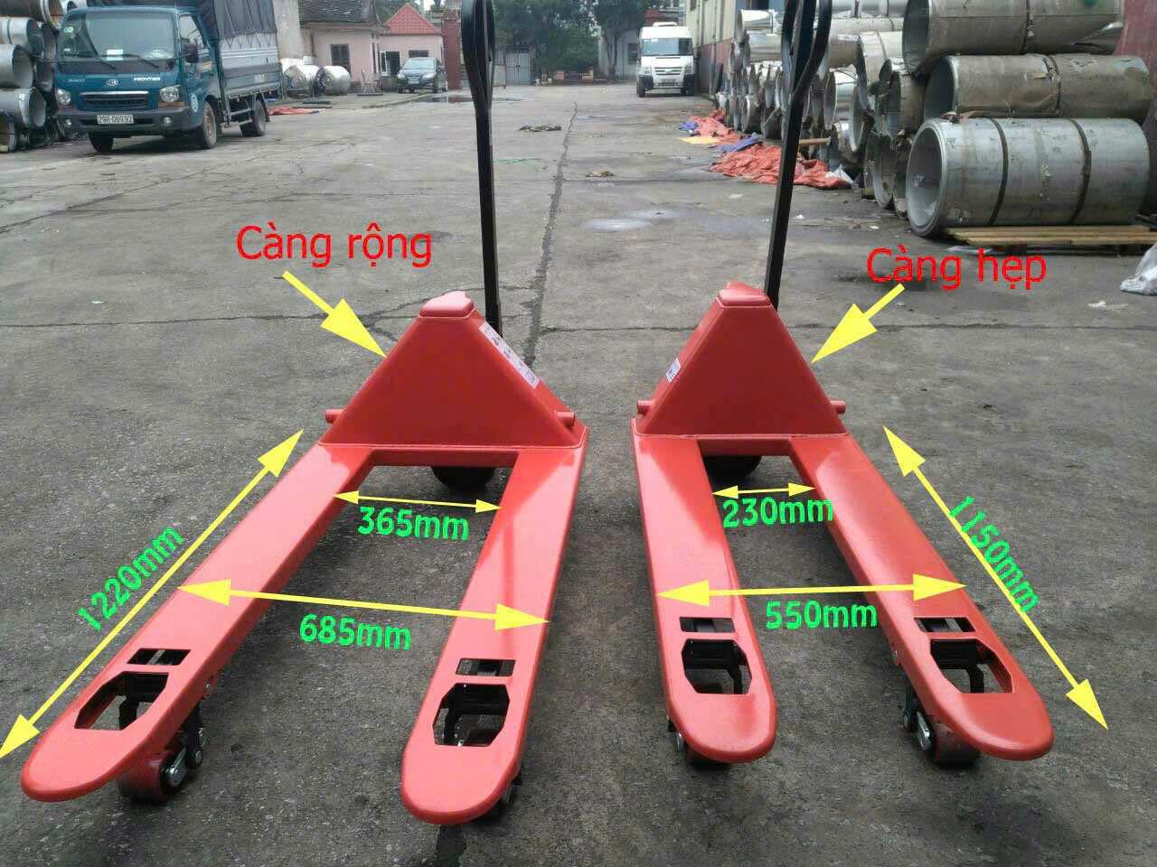 Xe nâng tay thấp càng rộng và càng hẹp màu đỏ đặt ngoài kho, có ghi kích thước chi tiết